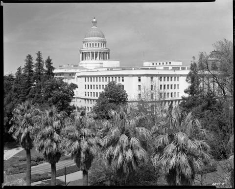 1952 photo of the exterior of the Capitol complex, taken from the top of a building at 12th and N Street, looking northwest toward newly constructed Annex.  1940s model truck seen in Capitol driveway.  Good view of the tree canopy of Capitol Park in the foreground (black and white photo).