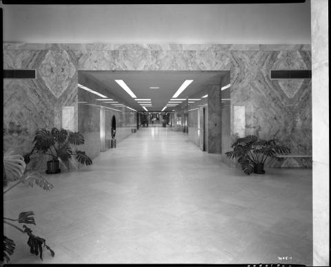 Photo of Capitol Annex hallway circa 1952, looking west toward rotunda.  Visible is the silver elevator bank display panel to the right and a State Police officer in hallway to the left.  Original glass doorway between rotunda and Annex is also visible in the distance (black and white photo).