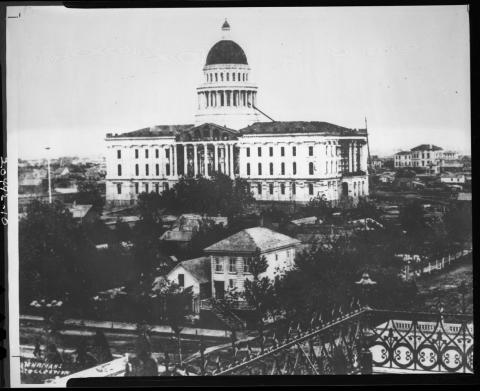 Photo of Capitol building under construction in the 1860s.  Photo taken from atop the Stanford Mansion (mansion’s ornate roof railing visible in foreground).