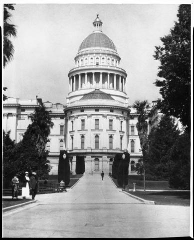 Early 20th century photo of Capitol apse, taken from center walkway in east Capitol Park.  Citizens are seen strolling the grounds.