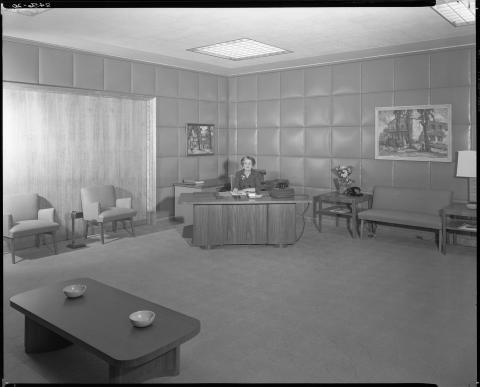 View of the Governor’s office public reception area, circa 1952.  Female secretary shown seated at desk. Wall is box stitched upholstered fabric. Also shown:  1950s era furniture and multiple ashtrays. Governor Earl Warren resigned the following year when he was appointed as Chief justice of the U.S. Supreme Court on October 5, 1953 (black and white photo).